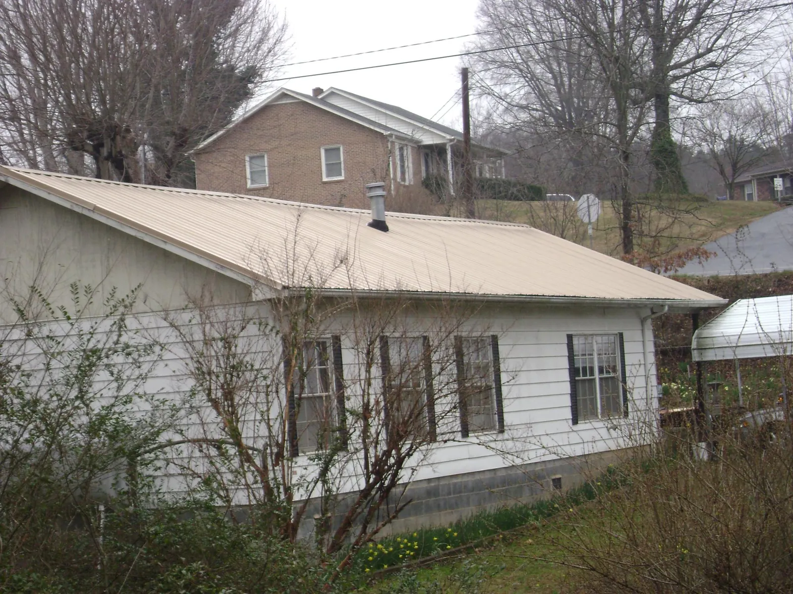 Tan metal roof on a white sided house set into a hillside — Commercial Roofing by Roofing Brothers in Johns Island
